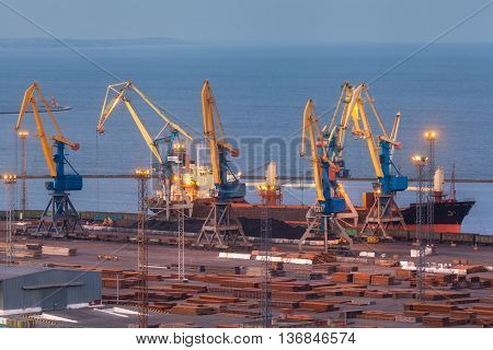 Sea commercial port at night in Mariupol Ukraine. Industrial view. Cargo freight ship with working cranes bridge in sea port at twilight. Cargo port logistic