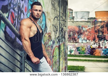 Handsome Muscular Hunk Man Outdoor in City Setting. Showing Healthy Body While Looking at Camera, Leaning against Graffiti Wall