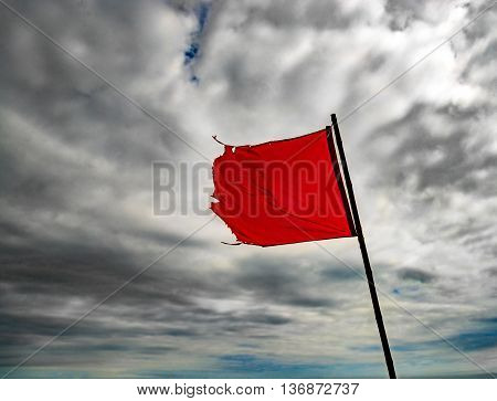 The wind blows a torn red flag under cloudy skies