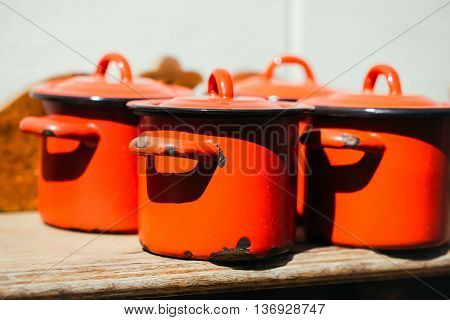 Cooking pots with lids orange enamel old outdoor on sunny day on wooden background