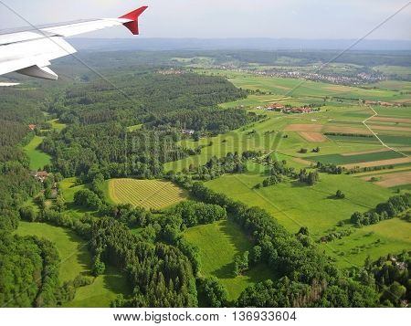 Typical german landscape forest and fields - aerial view from plane with visible wing during landing approach