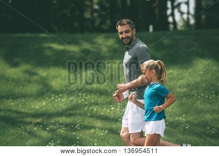Father and daughter jogging. Side view of cheerful father and daughter jogging in park together