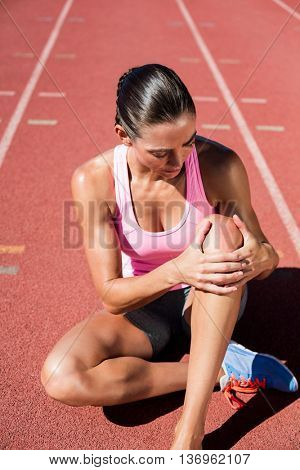 Female athlete with pain in knee joint on running track on a sunny day