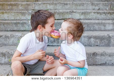 divide the a donut in half. two boys together bite from the donut. children enjoy a donut with strawberry frosting. feeding game for party