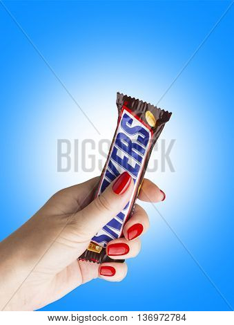 CHISINAU MOLDOVA - JULY 3 2016: Closeup of chocolate bar Snickers made by Mars Incorporated to a female hand. With clipping path