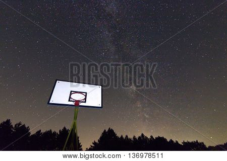 Basketball hoop and board under starry night. Milky way galaxy. Basketball court in night sky.