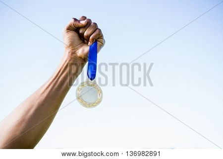 Close-up of athletes hand holding gold medal against sky