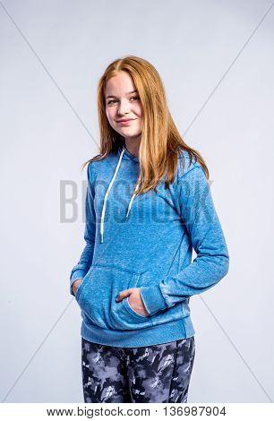 Teenage girl in blue sweatshirt and fitness leggings, hands in pockets, young woman, studio shot on gray background