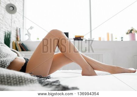 Perfect legs on bed with bent knees side view. Cropped image of erotically lying on bed beautiful woman in bedroom. Some free space