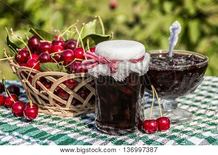 Cherry jam jar on background of basket of cherries and cherry jam