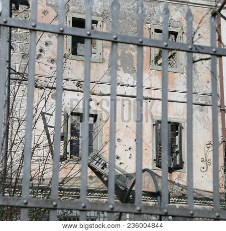 Abandoned Home Behind A Railing Of Iron With Broken Windows By War