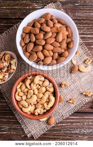 Differrent Variety Of Nuts - Walnuts, Cashew, Almond In Bowls. Rustic Scratched Wooden Table Backgro