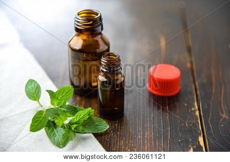 Essential Oil Of Peppermint In A Small Brown Bottle With Fresh Green Mint On An Old Wooden Backgroun