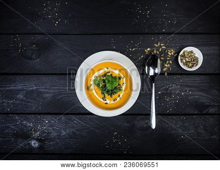 Pumpkin Soup With Jusai And Fried Cilantro, Served In White Bowl With A Spoon, On The Wooden Backgro
