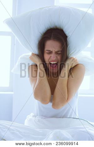 Young caucasian woman covering her head and ears with pillows