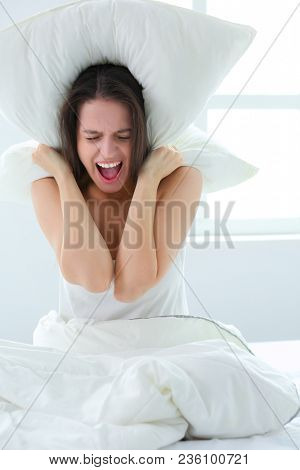 Young caucasian woman covering her head and ears with pillows