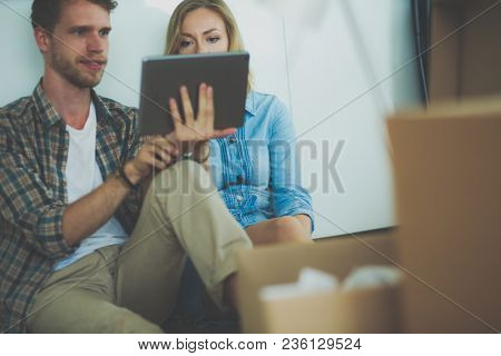 Young couple moving in new home.Sitting and relaxing after unpacking.Looking something on laptop. Young couple