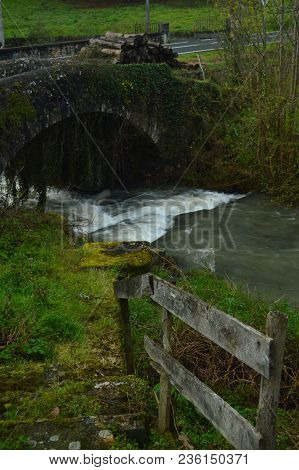 Beautiful Photo Postcard With A Brave River, A Roman Bridge And A Mountain Of Freshly Cut Logs Wet B