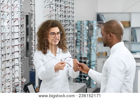 Young Ophthalmologist Helping To Choose Right Glasses From Transparrent Stand In The Ophthalmology S