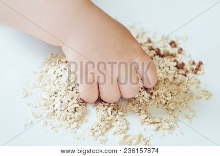 Baby Hand Closeup And Oat Flakes. Top View Background
