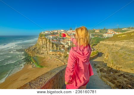 Blonde Woman Takes Photo Of Azenhas Do Mar On Atlantic Ocean. Female Tourist Takes Pictures By Mobil