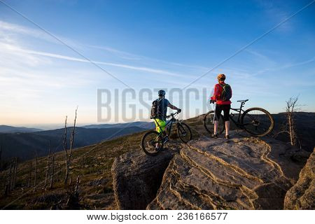 Mountain biking women and man riding on bikes at sunset mountains forest landscape. Couple cycling MTB enduro flow trail track. Outdoor sport activity.