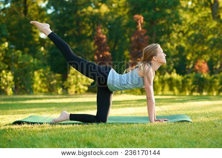 Sideview Of Girl Doing Stretching On The Park's Grass.