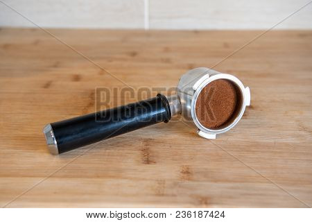 Portafilter With Temping Ground Coffee On Wooden Table.