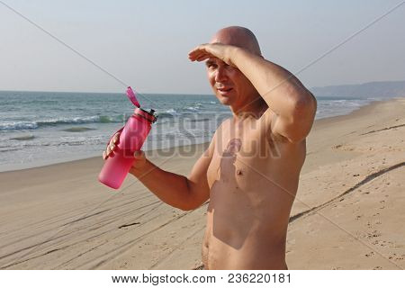 A Bald, Handsome Man With A Bare Or Bare Torso Is Drinking Water From A Pink Fitness Bottle. The Man