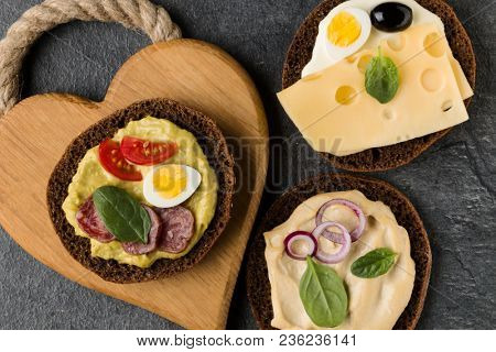 Open  faced  sandwich canape or crostini on a wooden serving board on dark stone background closeup. Top view.