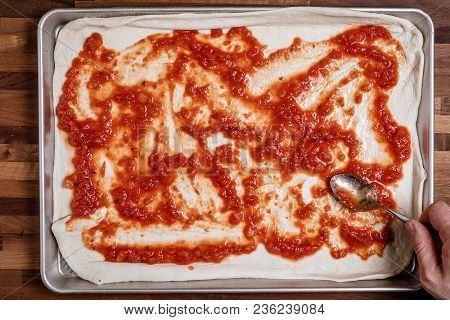 Man Spreading Tomato Sauce On Rolled Out Dough For Homemade Pizza