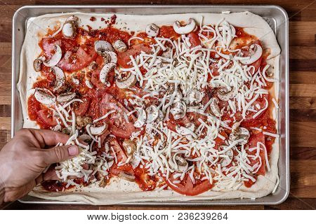 Man Spreading Shredded Cheddar Cheese On To Homemade Pizza