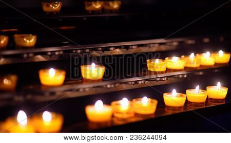 Close-up Photo Of Church Candles In Yellow Transparent Chandeliers With Dark Background