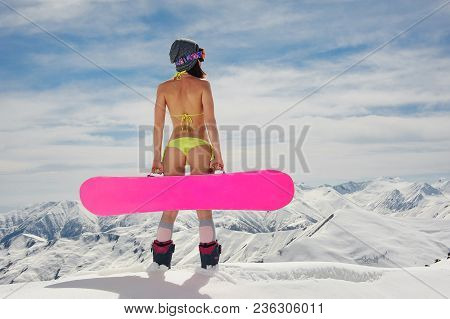 Back View Of Sexy Girl In A Swimsuit And Helmet Holding Pink Snowboard Standing On The Background Of