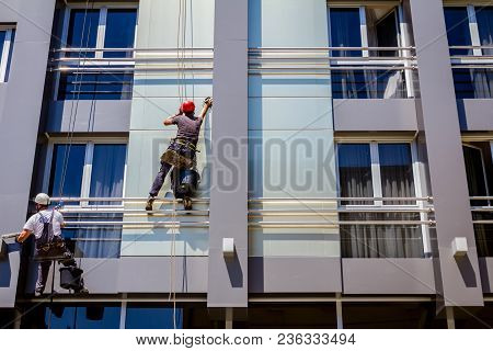 Two Industrial Climbers Are Washing, Cleaning Facade Of A Modern Office Building