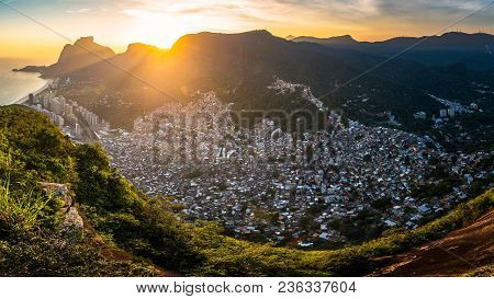 Panoramic View Of Rocinha, The Largest Favela In Rio De Janeiro City, By Sunset Behind Mountains