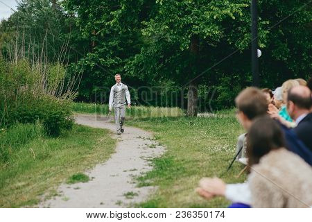 Groom In The Stylish Wedding Suit Going To The Bride With A Bouquet Of Flowers. Back View