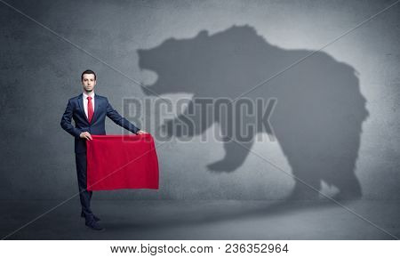 Businessman standing with red cloth in his hand and big bear shadow on his background