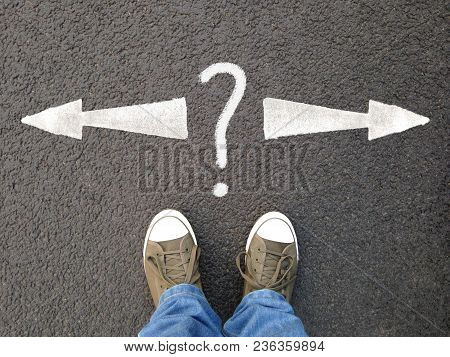 Feet In Canvas Shoes Standing On Asphalt From Personal Perspective, Road Markings With Arrows Pointi