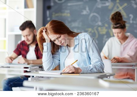 Confused student reading what she wrote in her copybook during individual work at lesson