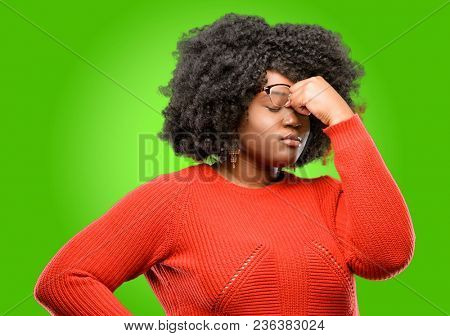 Beautiful african woman with sleepy expression, being overworked and tired, rubbes nose because of weariness