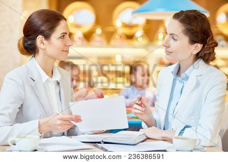 One of economists pointing at financail paper during discussion of its points in cafe on background of little girls