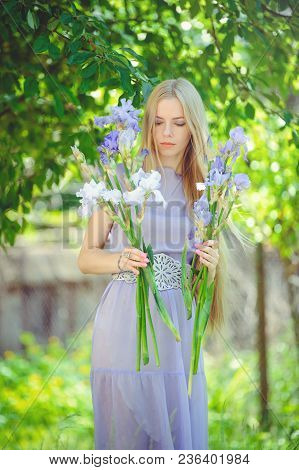 Attractive Young Girl With Blonde Dren Hair And Natural Make-up Smelling Blue Purple Iris Flowers On