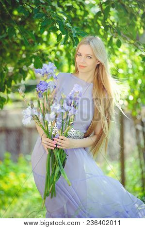 Attractive Young Girl With Blonde Dren Hair And Natural Make-up Smelling Blue Purple Iris Flowers On