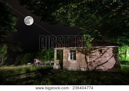 Mountain Night Landscape Of Building At Forest In Foggy Night With Moon. Green Meadow, Big Trees And