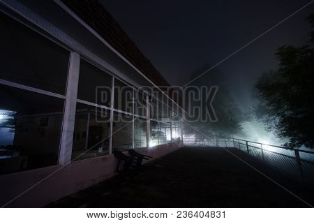 Mountain Night Landscape Of Building At Forest In Foggy Night With Moon. Green Meadow, Big Trees And