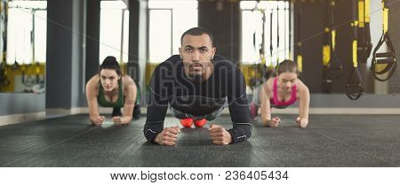 Fitness Group Doing Plank Workout Training With Coach Indoors. Young Men And Women Making Exercise A