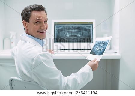 Feeling Happy. Exuberant Experienced Dentist Holding An Image And Working On Her Advanced Device