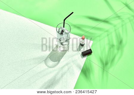 High Angle View Of Lipstick And Drinking Glass With Ice On Table. Green And White Background With Sh