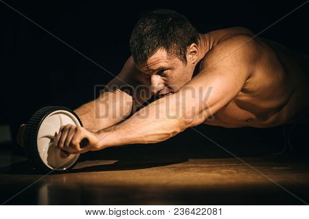A Fitness Man Shakes A Press With A Wheel. Isolated Dark Background